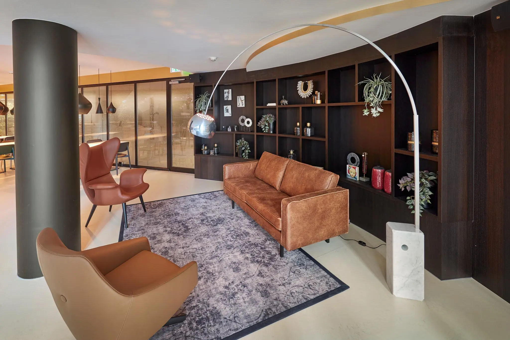 Moderne loungehoek aan de Fascinatio Boulevard met leren zitmeubilair, een vloerkleed, designlamp en een donkere wandkast met decoratie.